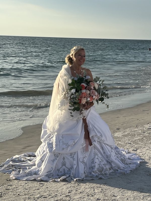 Bride smiling on a Florida beach in an altered white ballgown holding a bouquet