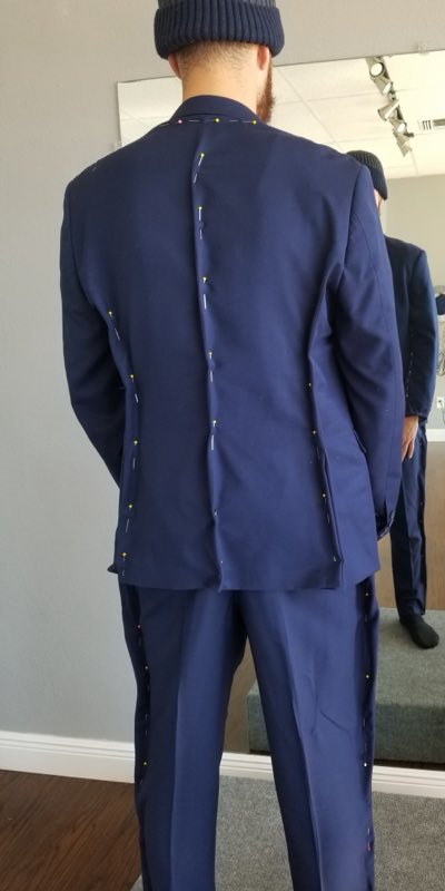 A navy suit jacket and trousers pinned along the seams during a fitting