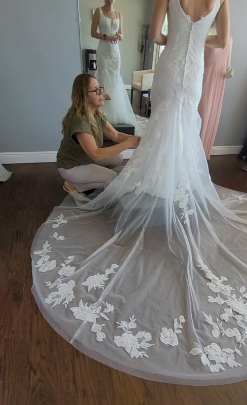 Ana Maria kneeling to fit the lace train of a wedding gown