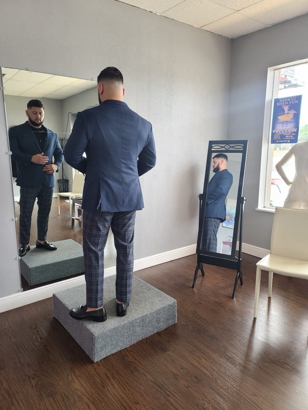 Man in a fitted navy suit and trousers standing on a fitting platform